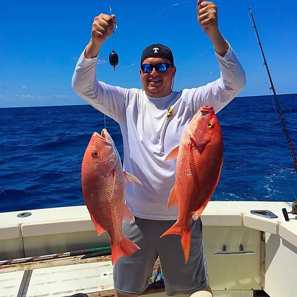 Man holding two red snapper aboard Triple Time.